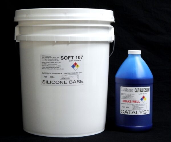 White plastic bucket labeled "44 lb Kit : Soft 107 – (7 shore A durometer) – Longer Pot Life Mold Making Silicone" next to a blue bottle of "cat blue solution catalyst" against a black background.