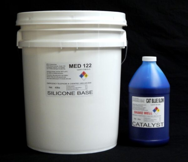 A white plastic bucket labeled "44 lb Kit : Medium 122 – (22 shore A durometer) – Longer Pot Life Mold Making Silicone" next to a blue bottle labeled "cat blue son catalyst" against a black background.