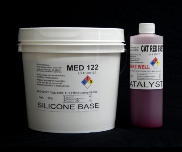 A large white bucket labeled "10 lb Kit : Medium 122 – (22 shore A durometer) – Fast Curing Mold Making Silicone" alongside a smaller bottle labeled "catalyst." both items have hazard symbols and black text on a black background.