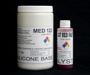 Two containers labeled "2 lb Kit : Medium 122 – (22 shore A durometer) – Fast Curing Mold Making Silicone" and "cat red fast catalyst" against a black background, displaying hazard and company information.