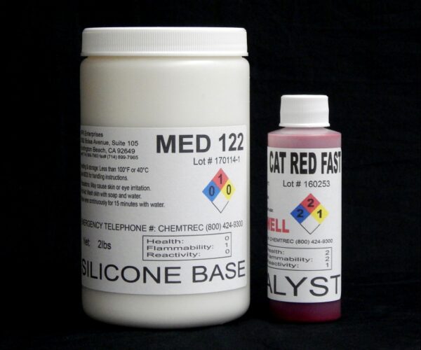 Two containers labeled "2 lb Kit : Medium 122 – (22 shore A durometer) – Fast Curing Mold Making Silicone" and "cat red fast catalyst" against a black background, displaying hazard and company information.