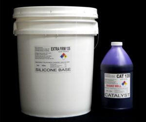 A white plastic bucket labeled "44 lb Kit : Extra Firm 135 – (35 shore A durometer) – Regular Pot Life Mold Making Silicone" and a purple bottle labeled "catalyst" against a black background.