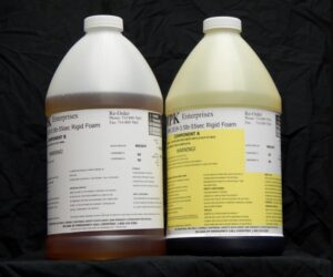 Two large plastic jugs of chemicals labeled "8 lb Kit : MPK-1019 : 3.5 lb Rigid Pour Foam" by pk enterprises, set against a black backdrop.