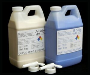 Two 10 lb Kit MPK 1125 Duplicating Silicone packaged in pourable 1/2 gal jugs with faucets labeled a and b, accompanied by measuring caps, against a black background.