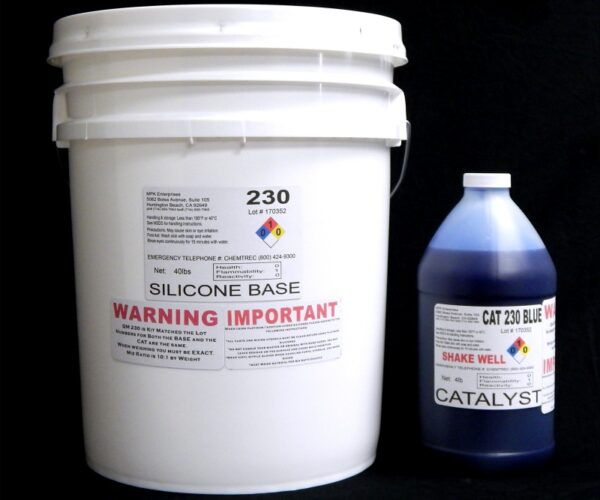 A white bucket labeled "44 lb Kit : QM 230 FG B: 30 shore A – Platinum Silicone" and a blue bottle labeled "Blue Catalyst" on a black background. both containers display hazard warnings and product information.