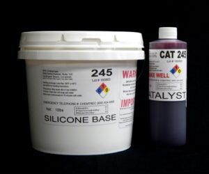 Large white bucket labeled "11 lb Kit : Food Grade QM 245 FG R: 45 shore A – Platinum Silicone" and smaller black bottle labeled "Red Catalyst" on a black background.